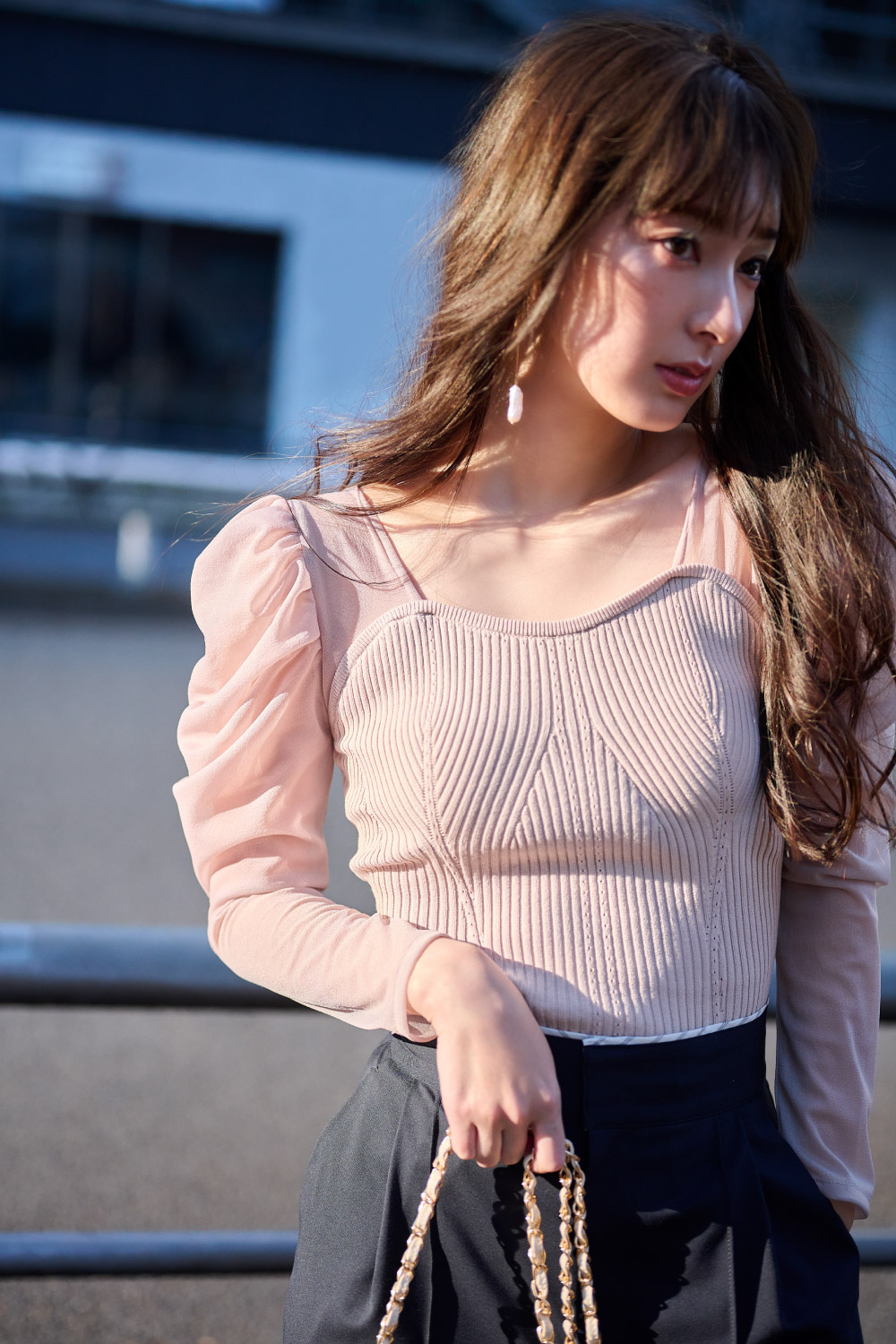 ピンクのニットブラウス・ブラックのパンツ・ホワイトのバッグを持った女性