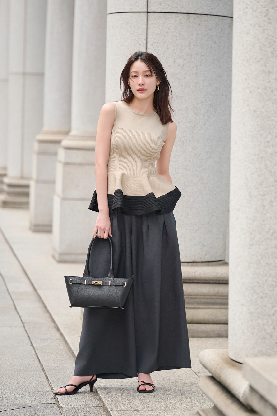 ベージュのペプラムトップス・黒のパンツを着用した女性